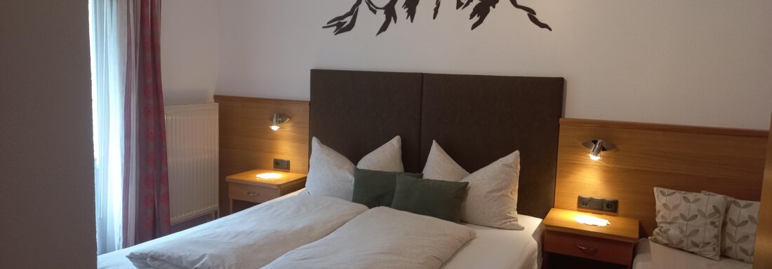 Ein gemütliches Schlafzimmer mit einem großen Bett und modernen Nachttischen. An der Wand befindet sich eine dekorative Bergsilhouette. - Apart Swoboda - Oetz