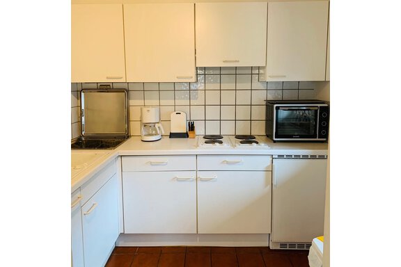 A modern, bright kitchen with white cabinets and a neutral tile pattern. Some kitchen appliances like a coffee maker and a microwave oven are visible. - Appartement Azalea - Oetz