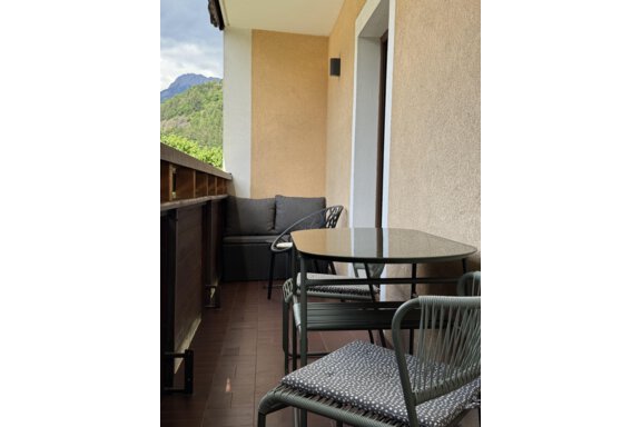 A cozy balcony with a table and chairs. In the background, green mountains are visible. - Appartements Schmid Peter - Oetz