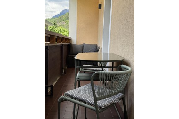 A cozy balcony with a table and two chairs. In the background, green mountains can be seen. - Appartements Schmid Peter - Oetz