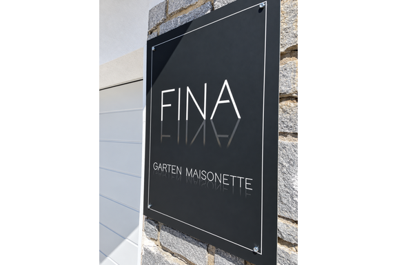 A modern, elegant sign with the inscription "FINA" and "GARTEN MAISONETTE". It is mounted on a stone wall and appears inviting. - Fina - Garten Maisonette - Oetz