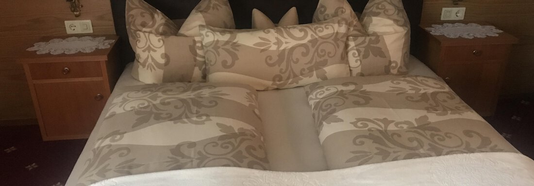 A cozy bedroom with a large bed and decorative pillows. The walls are made of wood, and there are two nightstands next to the bed. - Gästehaus Schrott - Oetz