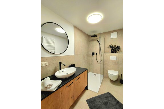 A modern bathroom with a shower and sink. The walls are painted in neutral tones and there is stylish lighting. - Haus Gstrein - Oetz
