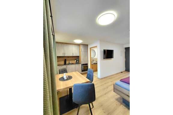 A modern furnished living and dining room with a kitchenette. The room has bright walls and a warm wooden floor. - Haus Gstrein - Oetz