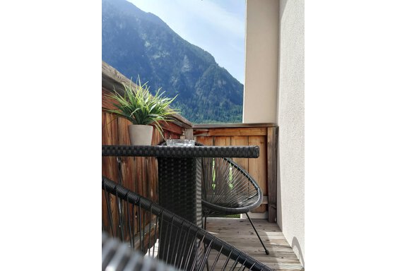 A cozy balcony with a table and a chair. In the background, mountains and a clear sky can be seen. - Haus Gstrein - Oetz