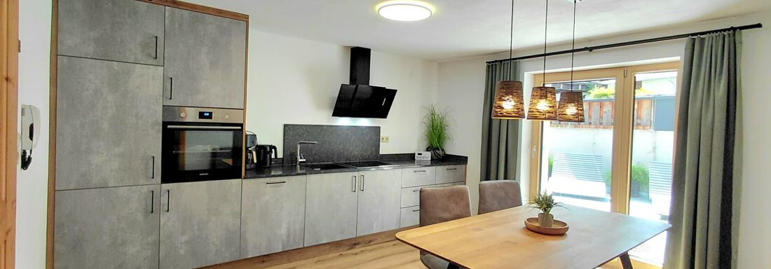 A modern kitchen with a dining table and chairs. Large windows let in a lot of daylight. - Haus Gstrein - Oetz