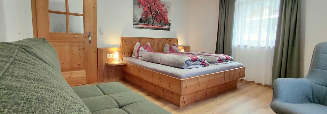 A cozy bedroom with a double bed and a green couch. The walls are light and the room has large windows that let in a lot of light. - Haus Gstrein - Oetz