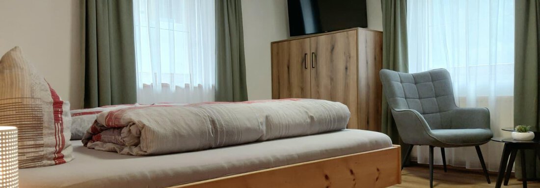 A cozy room with a large bed and a modern armchair. Bright curtains and a television complete the inviting atmosphere. - Haus Gstrein - Oetz