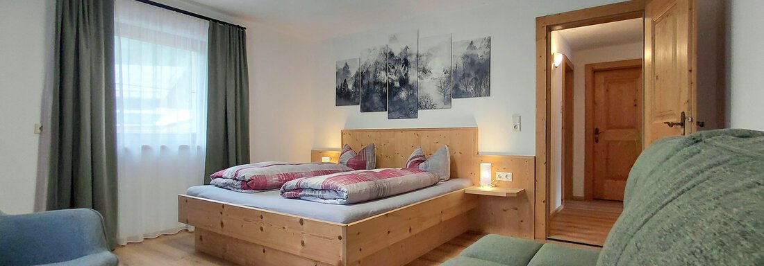 A modern bedroom with a double bed and a cozy seating area.  
Bright walls and natural light create an inviting atmosphere. - Haus Gstrein - Oetz