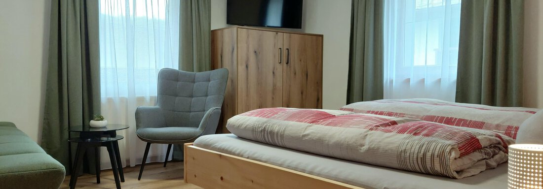 A cozy bedroom with a double bed and a television. The room is bright and modernly furnished, with a chair and a small table. - Haus Gstrein - Oetz