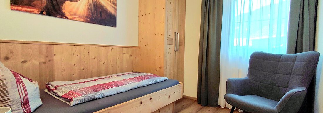 A cozy room with a single bed and a chair. The walls are made of wood and a large window lets in a lot of light. - Haus Gstrein - Oetz