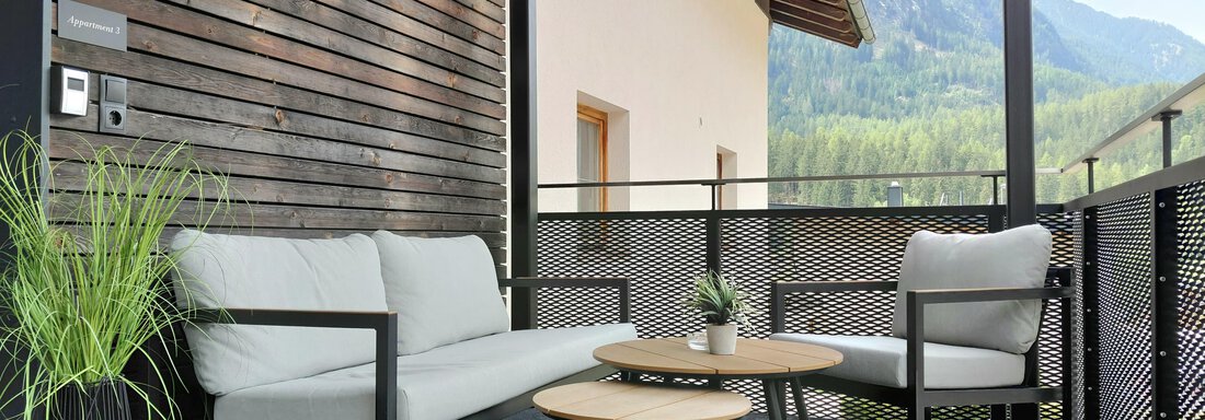 A modern balcony with comfortable furniture and a small table. In the background, mountains and a green landscape can be seen. - Haus Gstrein - Oetz