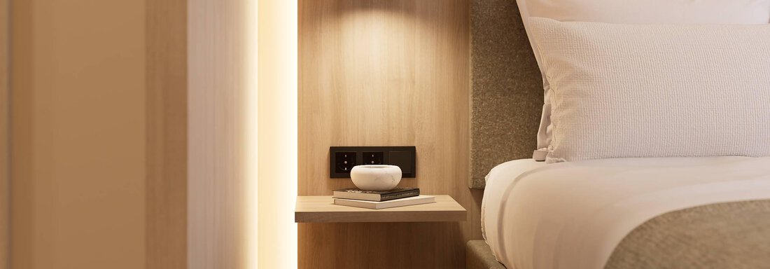 Ein modernes Schlafzimmer mit einem Bett und einem Nachttisch. Der Nachttisch hat eine Lampe und ein paar dekorative Gegenstände. - Hotel Marko - Oetz