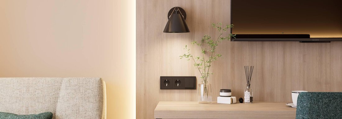 Ein modernes Zimmer mit einem gemütlichen Sessel und einem minimalistischen Schreibtisch. An der Wand hängt ein Fernseher, und eine kleine Pflanze sorgt für eine wohnliche Atmosphäre. - Hotel Marko - Oetz