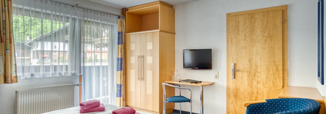 A cozy hotel room with two beds and colorful towels. There is a desk, two chairs, and a television on the wall. - Seehüter´s Hotel Seerose - Oetz