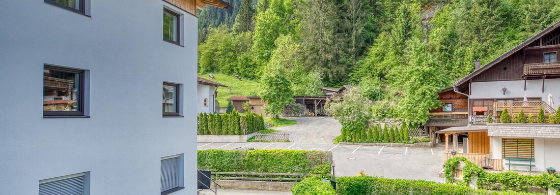 A picturesque landscape with green trees and mountains in the background. The image shows a quiet residential area with several buildings and a parking lot. - Seehüter´s Hotel Seerose - Oetz
