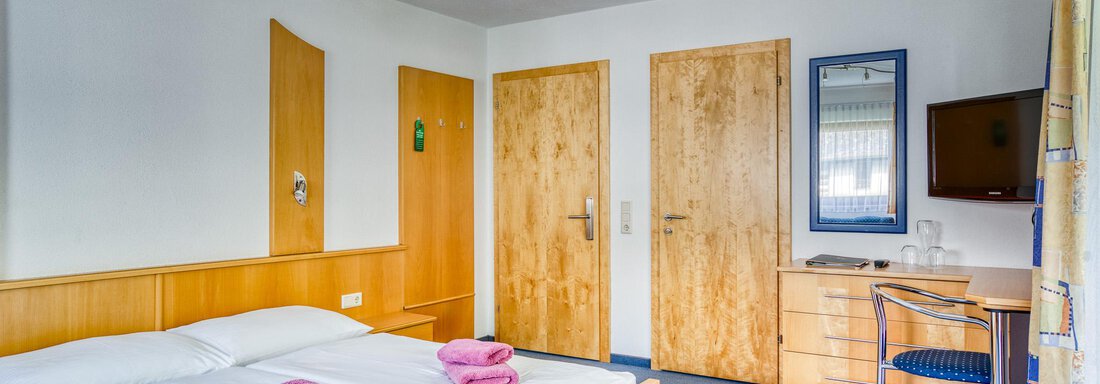 A cozy bedroom with two beds and colorful towels. There is a desk and a television on the wall. - Seehüter´s Hotel Seerose - Oetz