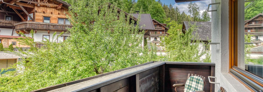 A balcony with two chairs and a view of green trees and traditional wooden houses. The surroundings are quiet and surrounded by mountains. - Seehüter´s Hotel Seerose - Oetz