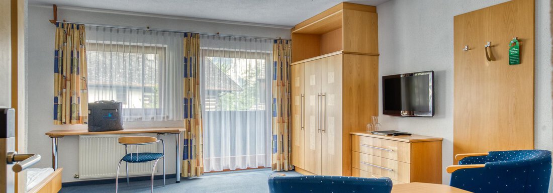 A cozy living space with blue carpet and two blue armchairs. There is a television and large windows that let in a lot of light. - Seehüter´s Hotel Seerose - Oetz