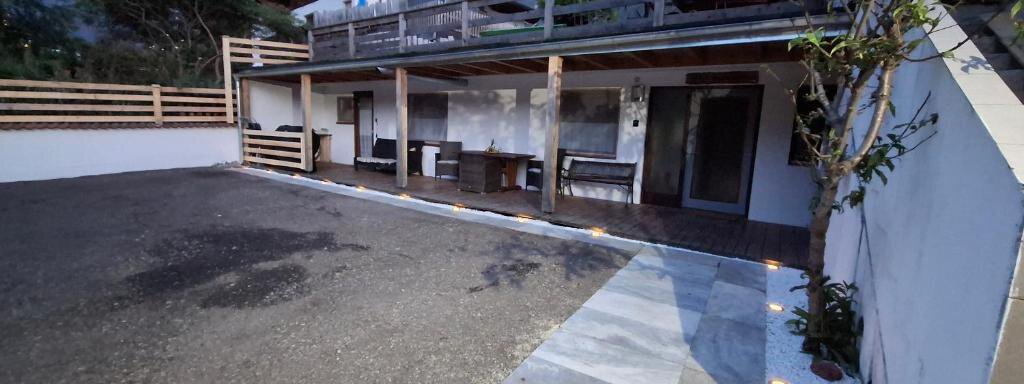 A modern outdoor area with a concrete floor and a covered terrace. In the background, trees and mountains are visible. - Appartement Harmony - Sautens