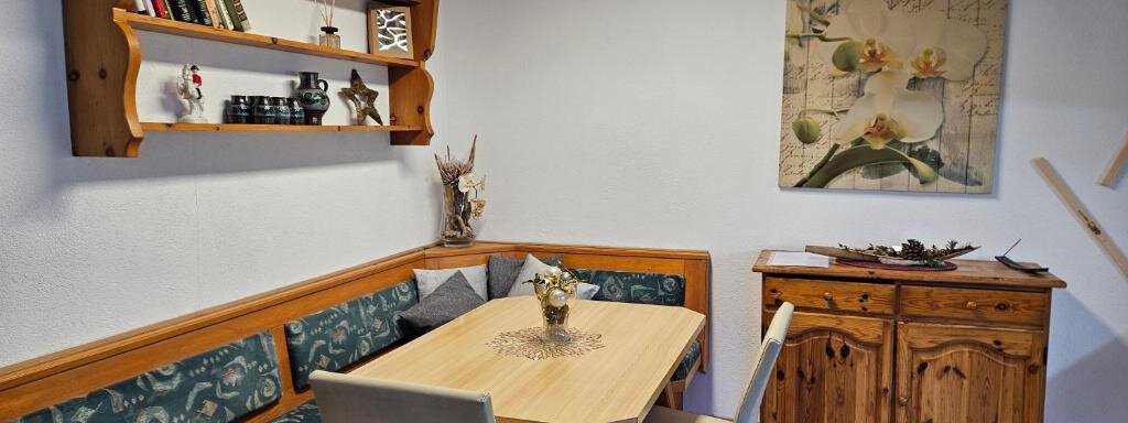 A cozy dining area with a wooden table and benches. On the wall are bookshelves and a decorative picture with flowers. - Appartement Harmony - Sautens
