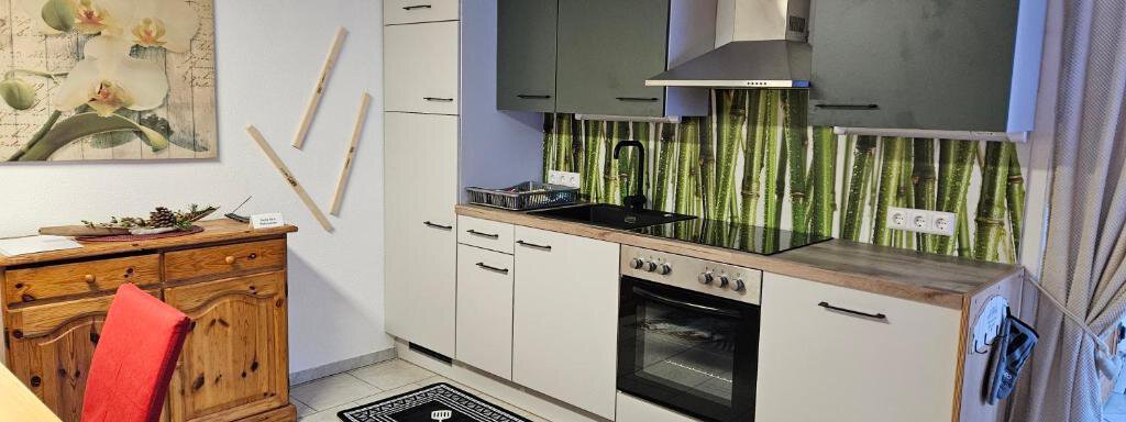 A modern kitchen with an elegant design and a green bamboo background. A table with red chairs and a dresser complement the space. - Appartement Harmony - Sautens