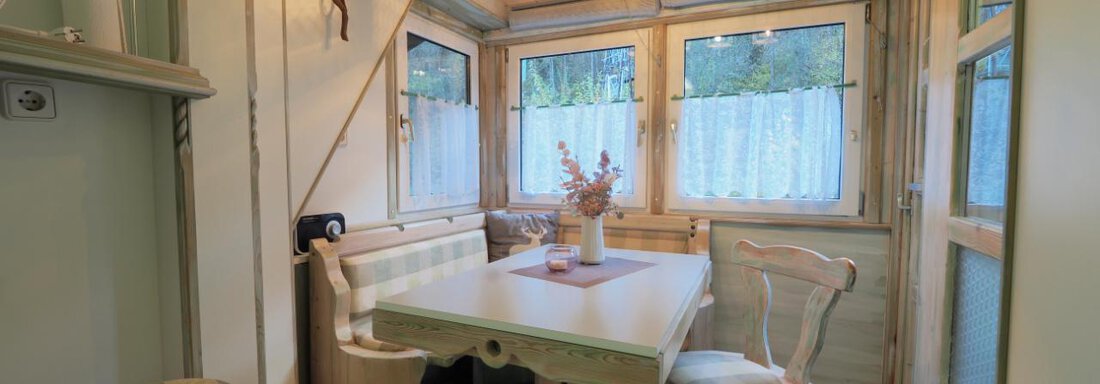 Ein gemütlicher Essbereich mit einem weißen Tisch und Stühlen aus Holz. Große Fenster lassen viel Tageslicht herein, und eine Vase mit Blumen schmückt den Tisch. - bei Herrmann´s - Sautens