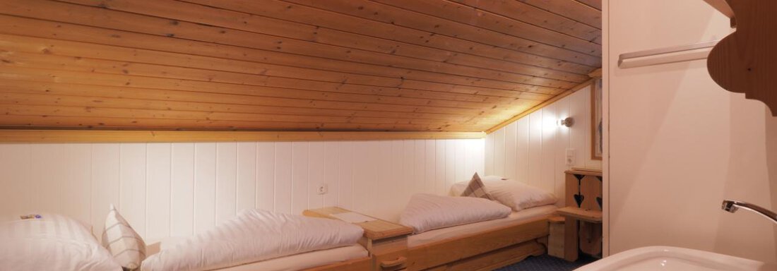 Ein gemütliches Dachzimmer mit Holzdecken. Zwei Einzelbetten und ein Waschbecken sind sichtbar. - bei Herrmann´s - Sautens