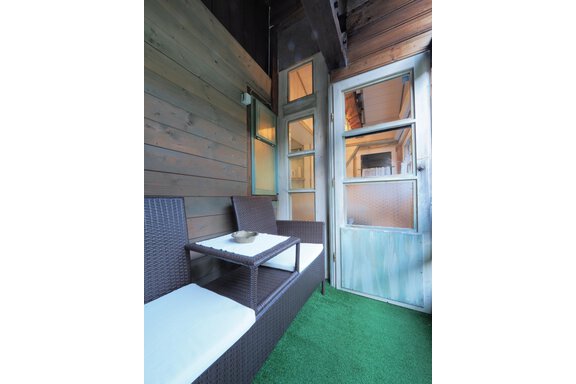 Ein gemütlicher Balkon mit einem Rattanset und einem kleinen Tisch. Die Wände sind aus Holz und die Tür ist aus Glas. - bei Herrmann´s - Sautens
