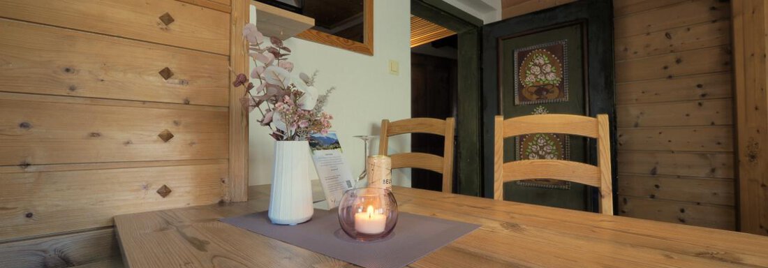 Ein gemütlicher Tisch aus Holz mit Stühlen in einem rustikalen Raum. Eine Kerze und eine Vase mit Trockenblumen verleihen eine einladende Atmosphäre. - bei Herrmann´s - Sautens