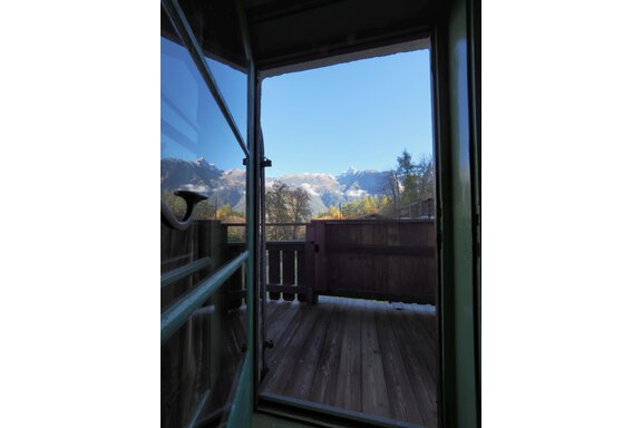 Ein Blick durch eine offene Tür auf einen Balkon. Im Hintergrund sind majestätische Berge und ein klarer blauer Himmel zu sehen. - bei Herrmann´s - Sautens