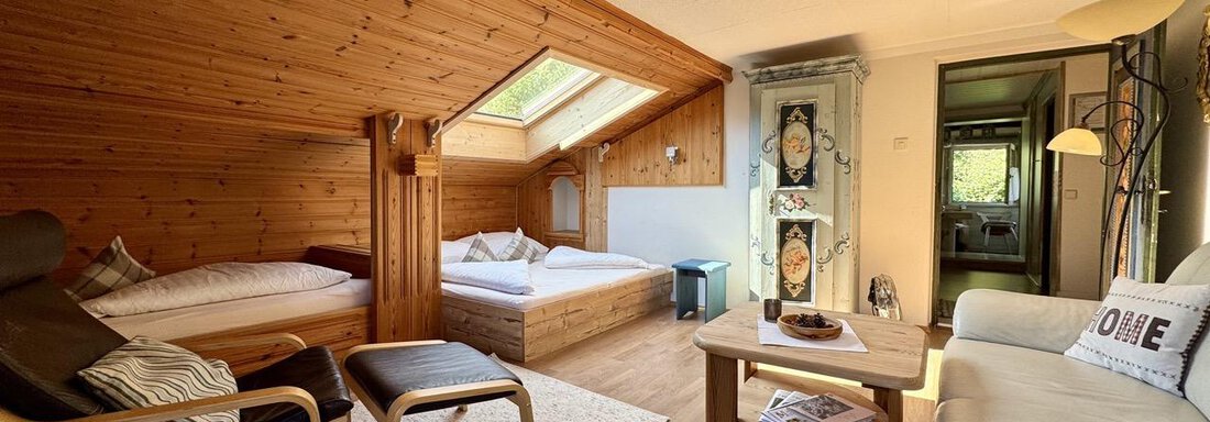 Ein gemütliches Zimmer mit Holzwänden und einem Dachfenster. Es gibt ein Sofa, zwei Betten und einen Tisch mit Stühlen. - bei Herrmann´s - Sautens