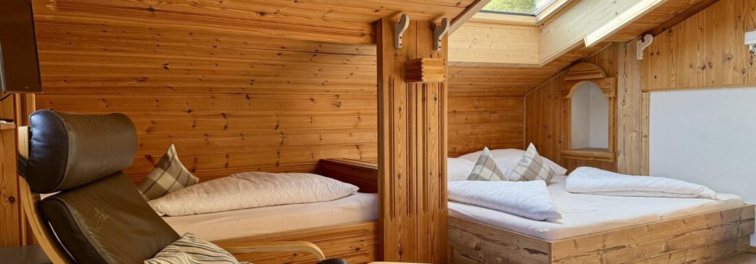 Ein gemütliches Dachzimmer mit Holzvertäfelung und zwei Betten. Ein bequemer Sessel und ein Hocker laden zum Entspannen ein. - bei Herrmann´s - Sautens