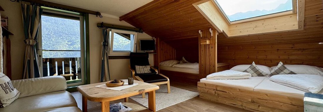 Ein gemütliches Zimmer mit Holzwänden und einem großen Fenster. Es gibt ein Doppelbett, eine Couch und einen Tisch. Das große Dachfenster mit Blick auf den Acherkogel ist mit einem UV Rollo gegen direkte Sonneneinstrahlung geschützt. - bei Herrmann´s - Sautens