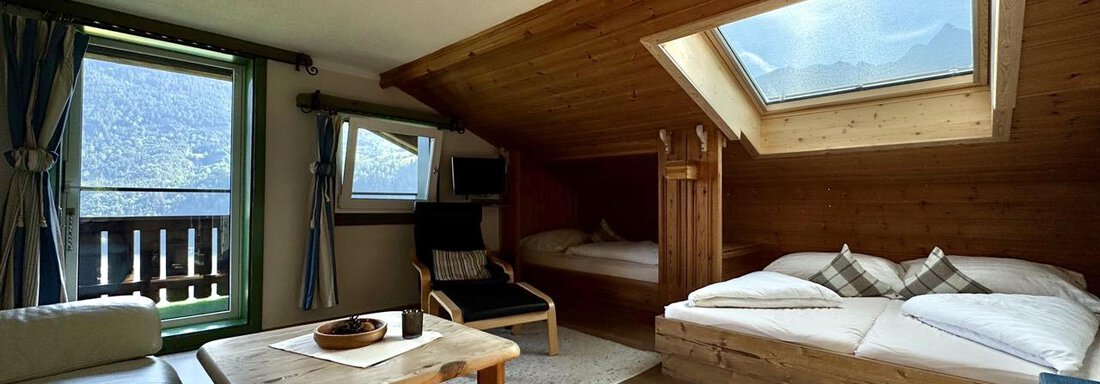 Ein gemütliches Dachzimmer mit Holzverkleidungen und Fenstern, die einen Blick auf die Berge bieten. Es gibt ein Doppelbett, ein Einzelbett und eine kleine Sitzecke. - bei Herrmann´s - Sautens