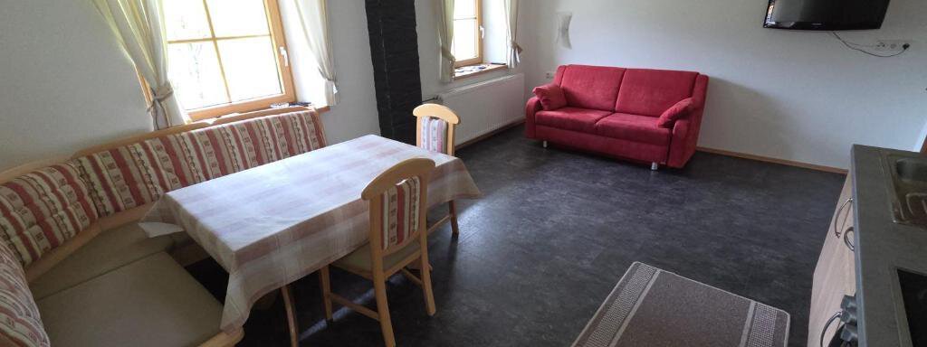 A cozy living space with a dining table and a red sofa. Large windows provide plenty of daylight. - Ferienhof Strigl - Sautens