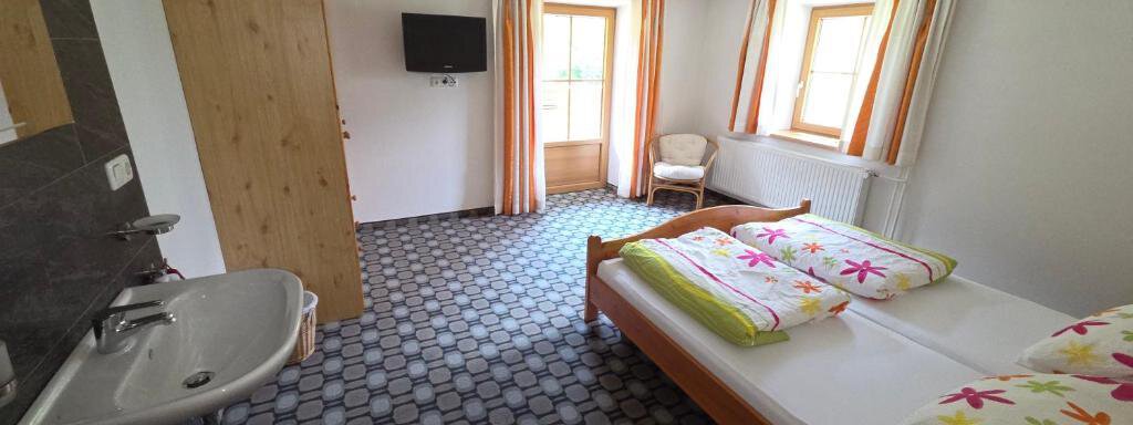 A simple, bright bedroom with two beds and colorful pillows. There is a television, a chair, and a window with a view outside. - Ferienhof Strigl - Sautens