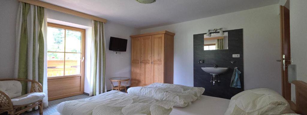 A cozy room with two beds and large windows. There is a wardrobe and a television, as well as a modern sink. - Ferienhof Strigl - Sautens