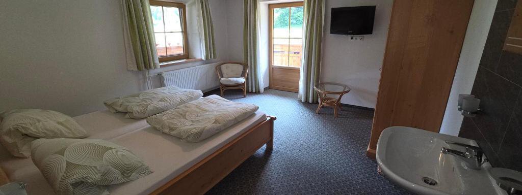 A simple bedroom with two beds, a desk, and a window. The room contains wooden furniture as well as a television on the wall. - Ferienhof Strigl - Sautens