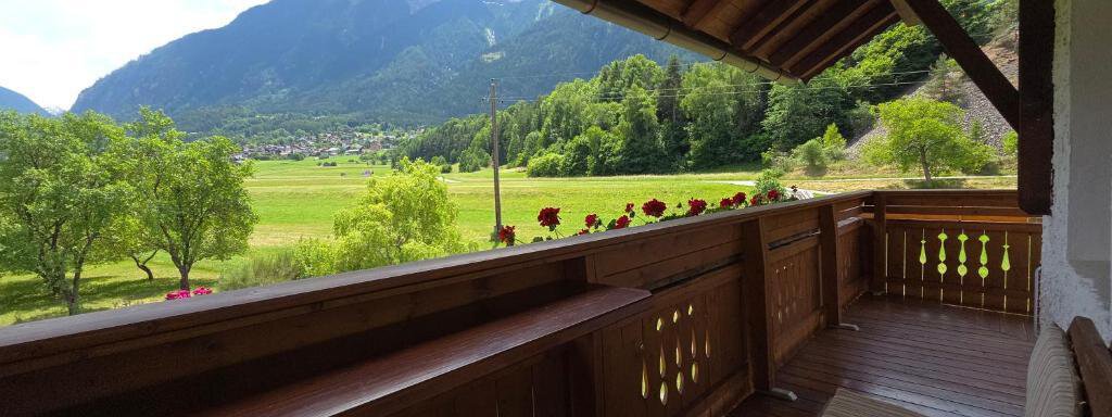 A beautiful balcony with rustic wooden cladding and a view of a green landscape. In the background, mountains and a blue sky can be seen. - Ferienhof Strigl - Sautens