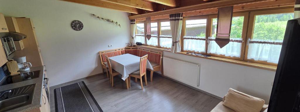 A cozy kitchen with a dining table and wooden shelves. Large windows provide plenty of daylight and a view of the greenery. - Ferienhof Strigl - Sautens