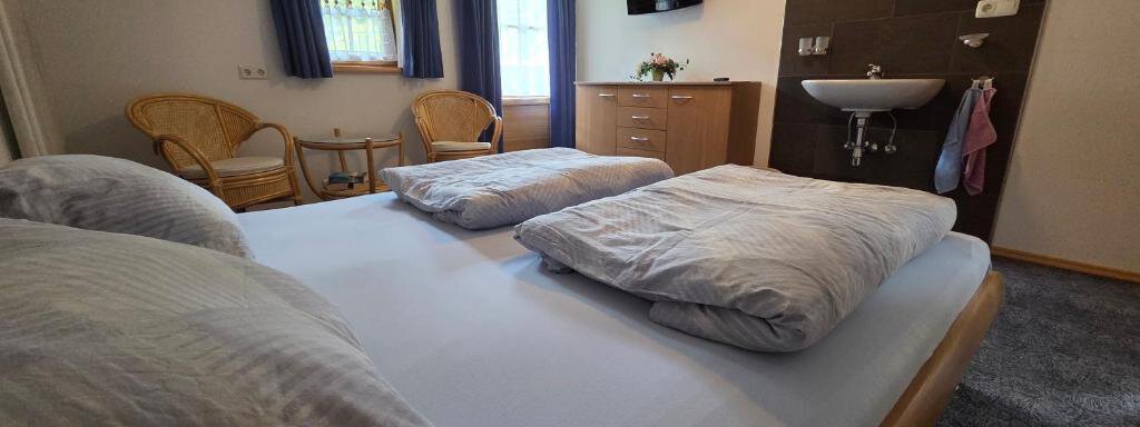 A cozy bedroom with a large bed and two pillows. There is a television, a washing facility, and two wicker chairs next to the window. - Ferienhof Strigl - Sautens