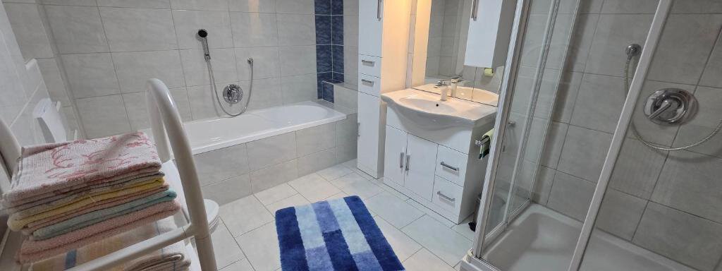 A modern bathroom with a bathtub and a walk-in shower. Towels are neatly stacked and a vanity with a mirror is present. - Ferienhof Strigl - Sautens