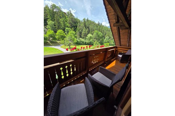 A cozy balcony with two rattan chairs and a beautiful view of green trees and flowers. The sky is clear and sunny. - Ferienhof Strigl - Sautens