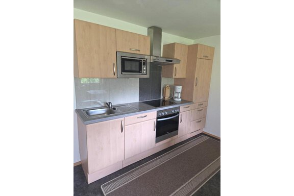 A modern kitchen with bright wooden cabinets and a stainless steel sink. The kitchen features a stove, an oven, and a microwave. - Ferienhof Strigl - Sautens