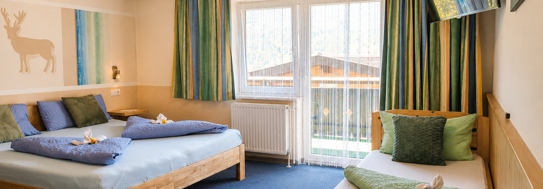A cozy room with two beds and a single bed. Large windows provide plenty of daylight and a view of nature. - Gästehaus Fernblick - Sautens