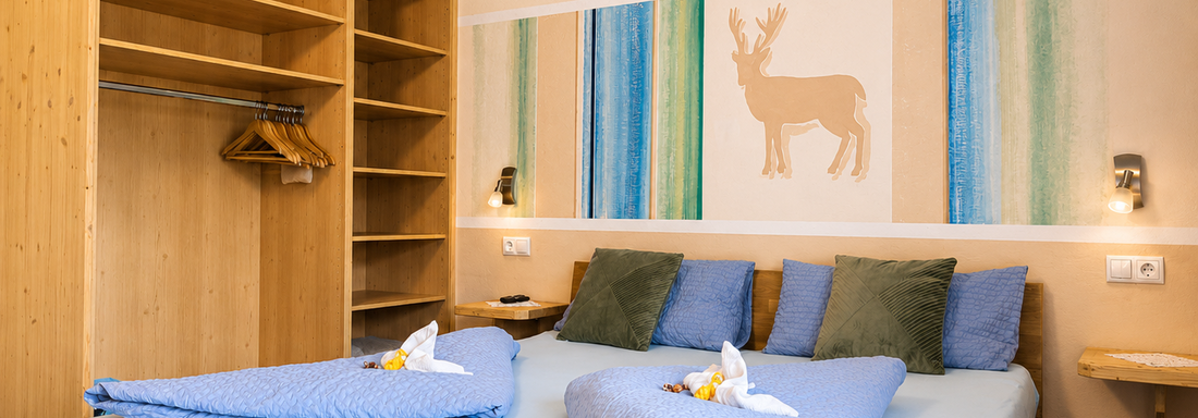A cozy bedroom with a large bed and decorative cushions. On the wall, there is a stylized reindeer motif in soft colors. - Gästehaus Fernblick - Sautens