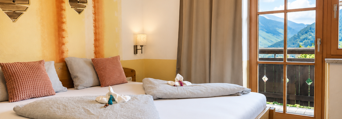 A cozy bedroom with a large bed and bright furniture. Through the window, you can see the mountains and the blue sky. - Gästehaus Fernblick - Sautens