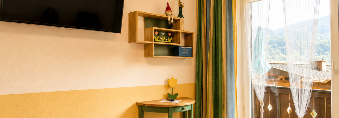 A cozy room with a table and chairs. A transparent curtain hangs at the window and a television is mounted on the wall. - Gästehaus Fernblick - Sautens