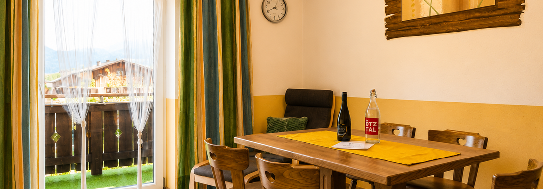A cozy dining area with a wooden table and chairs. Large windows bring in plenty of light and offer a view of the landscape. - Gästehaus Fernblick - Sautens